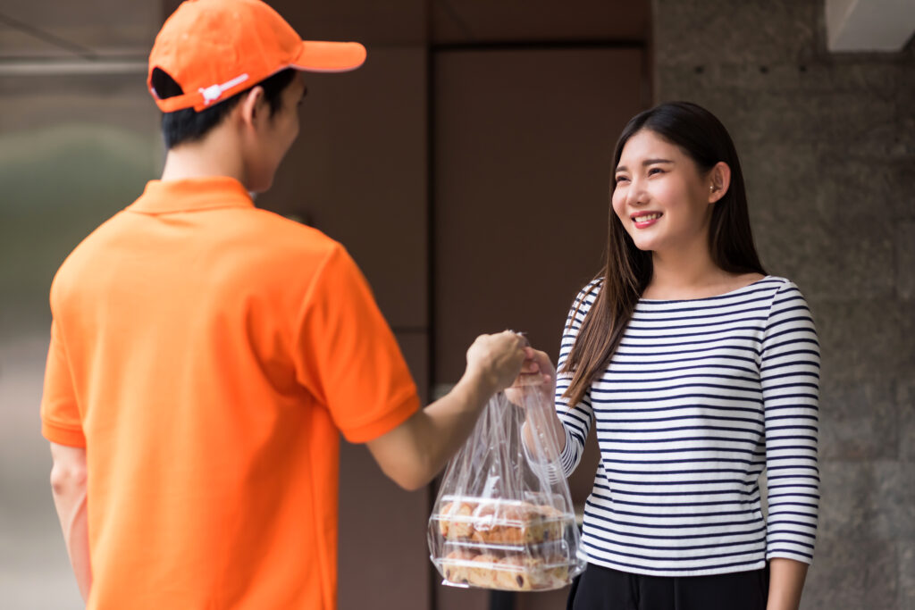 Deliveryman in uniform give bakery to smiling asian customer