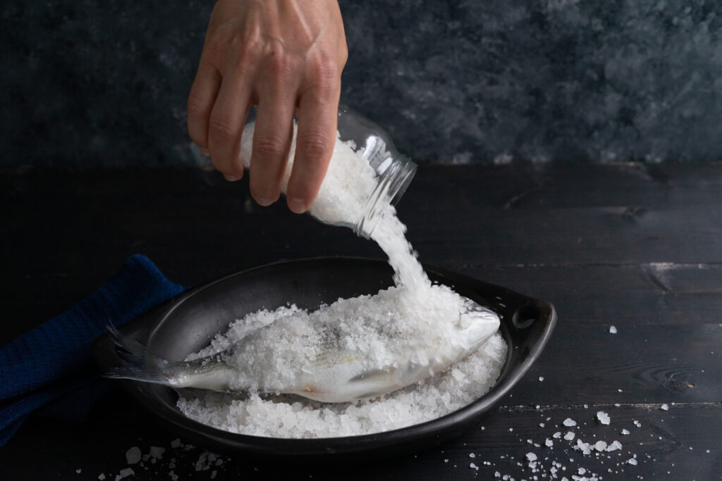 Process of preparation of sea bream salt. sparus aurata top view. dark background.