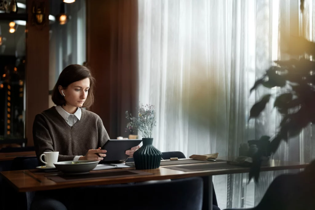 一名女性在室內空間中使用平板電腦閱讀資料，桌上擺放咖啡與文件，呈現專注思考與規劃生活的情境。